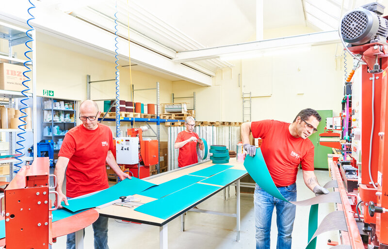 Schleifmittel Converting Abgebildet ist die Verarbeitung/das Converting von Schleifmitteln in de IBZ Produktion. Dabei wird das Schleifmittel den Bedürfnissen der Kunden angepasst. Auf dem Bild sind zwei Männer zu sehen,