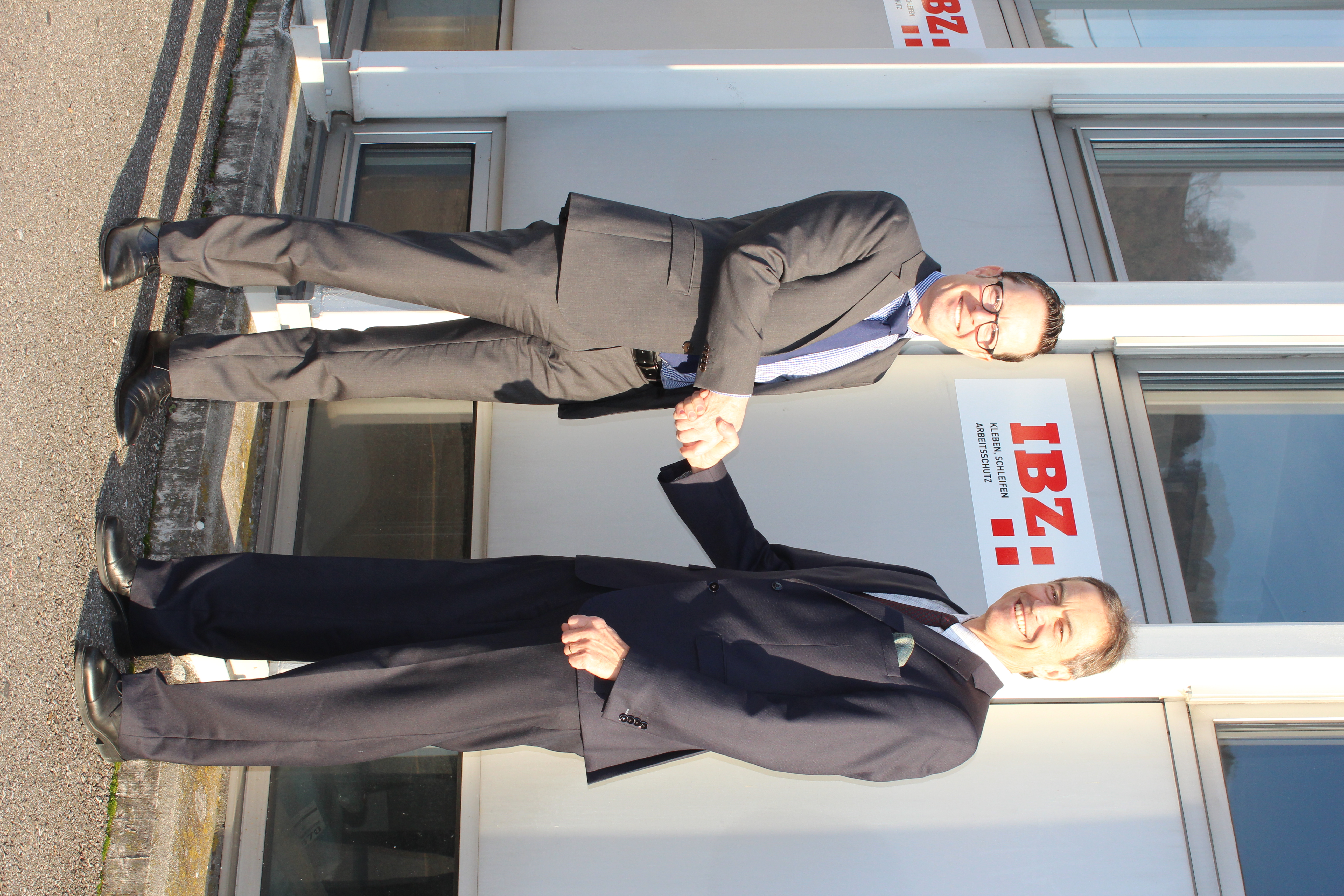 Remise des clés de l'IBZ Industrie AG entre Urs Egli et Roger Fehlmann. Les deux se tiennent devant le bâtiment de l'IBZ Industrie AG et se serrent la main.