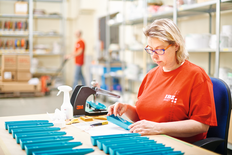 Abbildung Ausrüsten für die Firmenbroschüre IBZ Industrie AG. Frau ist im Lager abgebildet, wie sie blaue Produkte ausrüstet.