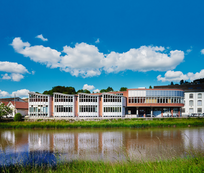 Bâtiment d'IBZ Industrie AG vu de l'autre côté de la rivière. Le bâtiment est entièrement représenté derrière la Sihl et sous le ciel bleu.