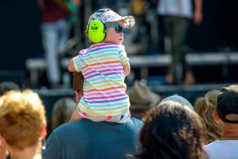 L'image montre un enfant de dos portant une chemise colorée sur les épaules de son père. En plus de la protection auditive 3m, l'enfant porte des lunettes de soleil et un chapeau.